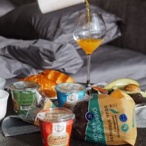 Cozy breakfast setup with croissant, juice, and yogurt on bedside table, creating a relaxing morning vibe.