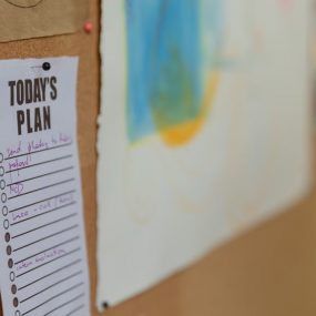 Close-up of a corkboard with a to-do list and colorful artwork in an office setting.